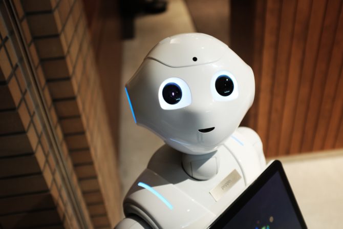 A robot looking at the camera while holding a tablet computer