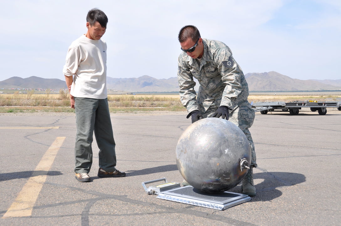 A Local Person Observes An Army Personal Standing At The Chinggis Khaan International Airport, Mongolia Weighing A Hydrogen Fuel Tank