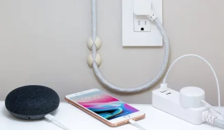 A photo of iPhone 8 Plus with Google Home Mini and a power extension plugged in socket showing smart and secure home