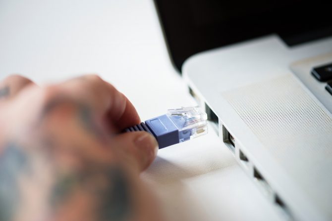 A Hand Plugging In An Ethernet Port To The Laptop