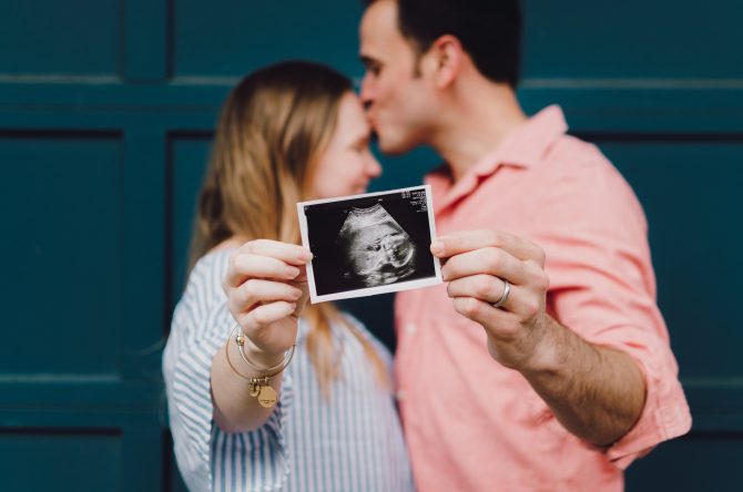 A Husband Kissing Her Wife, Showing Ultrasound Of Their Baby