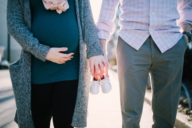 A Photo Of Husband And A Pregnant Wife Holding Hands And Pair Of Shoes For A Child