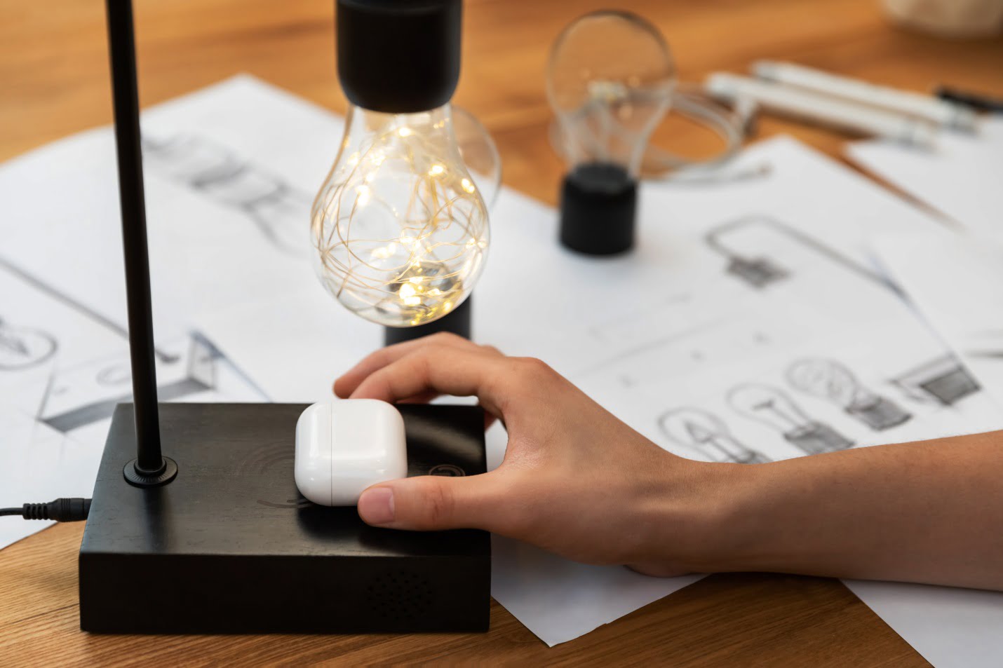 A Woman Is Placing Her Airpods To Wirelessly Charge On Gravita Lamp